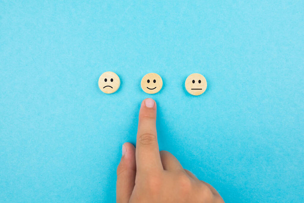 Konzepte der Kundendienstbewertung und der Zufriedenheitsbefragung. Die Hand des Kunden wählte ein Symbol für ein glückliches Gesicht. Blauer Hintergrund. - Foto, Bild