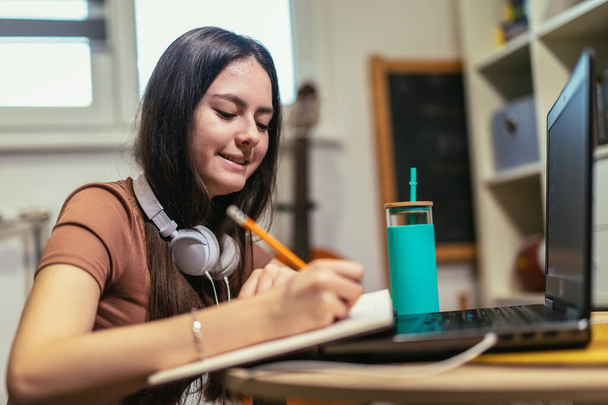 Teen girl school student wear headphone write notes watch video online webinar learn on laptop - Фото, изображение
