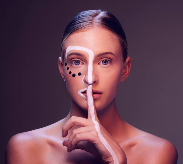 Woman, face and paint in finger, lips or studio for art, secret or cosmetic for fantasy by dark background. Girl, model and facial painting with hush sign, mouth or creativity with makeup in portrait. - Photo, Image