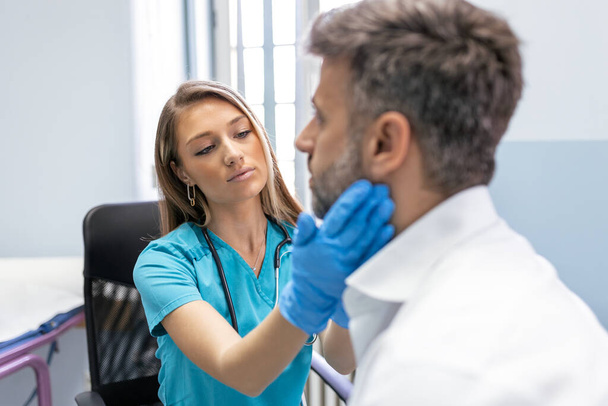 Concept of professional consultation in therapist system. Close up portrait of doctor woman examining tonsils of man in medical office - Photo, Image