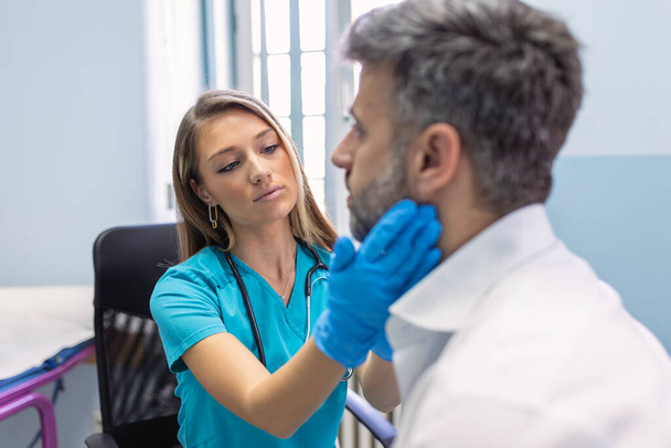 Endocrinologist examining throat of man in clinic. Men with thyroid gland test . Endocrinology, hormones and treatment. Inflammation of the sore throat - Photo, Image