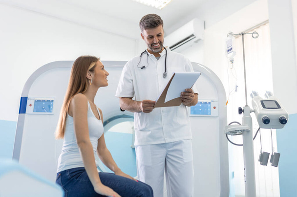 Male doctor giving information to woman before MRI scan examination. Magnetic resonance imaging technology in specialized medical clinic. - Photo, Image