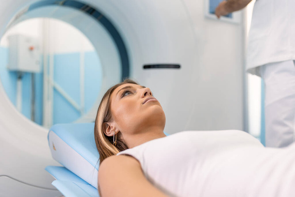 Paciente feminina deitada em uma cama de tomografia computadorizada ou PET ou ressonância magnética, movendo-se para dentro da máquina enquanto ela varre seus parâmetros cerebrais e vitais. - Foto, Imagem