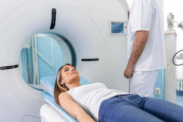 De patiënt ligt op CT of MRI, het bed wordt verplaatst in de machine, het scannen van haar lichaam en hersenen onder toezicht van een arts, radioloog. In een medisch laboratorium met hightech apparatuur. - Foto, afbeelding