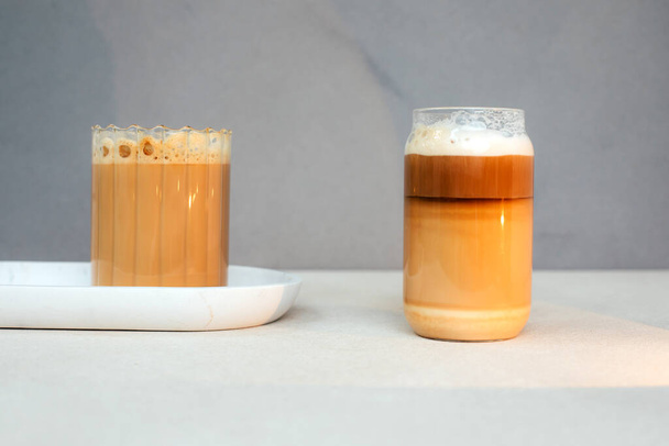 Sütlü kahve, kapuçino şeffaf cam bardakta köpüklü latte ve açık beton arka plan. Ön görünüm - Fotoğraf, Görsel