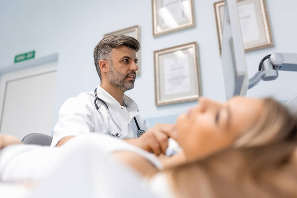 Foto ravvicinata di una giovane donna che si fa visitare il collo dal medico usando uno scanner ad ultrasuoni in una clinica moderna
. - Foto, immagini