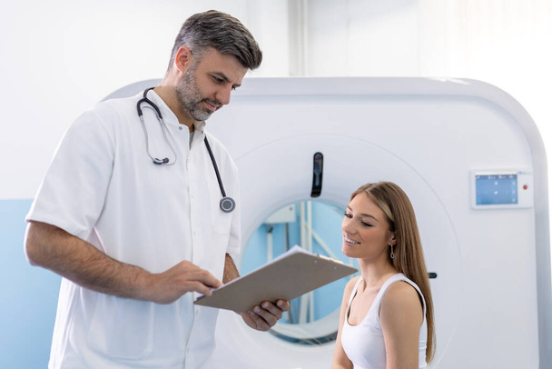 Pacjentka zajmująca miejsce i zadająca pytania na temat tomografii komputerowej lekarzowi uprawnemu po przeprowadzeniu badania w nowoczesnym szpitalu - Zdjęcie, obraz