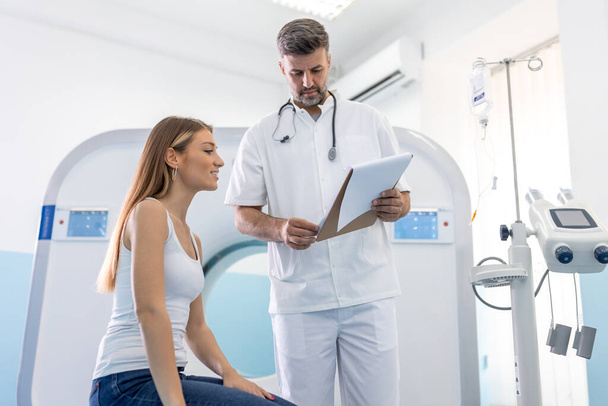 Male doctor giving information to woman before MRI scan examination. Magnetic resonance imaging technology in specialized medical clinic. - Photo, Image
