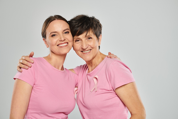 Brustkrebs-Konzept, glückliche zwei Frauen, die in die Kamera schauen und sich vor grauem Hintergrund umarmen, Unterstützung - Foto, Bild