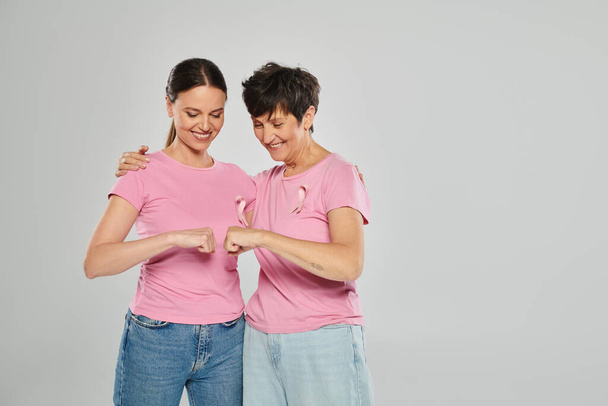 koncepce rakoviny prsu, šťastné ženy s růžovými stuhami pěsti narážející na šedé pozadí, bez rakoviny - Fotografie, Obrázek