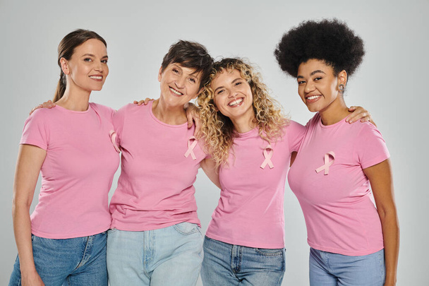 consapevolezza del cancro al seno, allegre donne interrazziali con nastri rosa che si abbracciano sul grigio, diversità - Foto, immagini