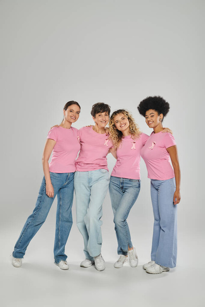 Brustkrebs-Bewusstsein, fröhliche multikulturelle Frauen mit rosafarbenen Bändern, die sich auf Grau umarmen, Vielfalt - Foto, Bild
