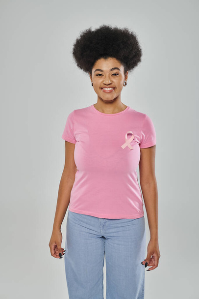 乳がんに対する意識,灰色の背景,多様性,笑顔にピンクのリボンを持つアフリカ系アメリカ人女性 - 写真・画像