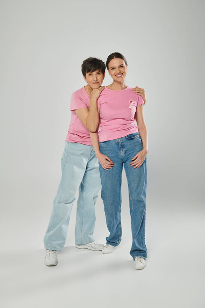 glückliche Frauen mit rosa Schleifen vor grauem Hintergrund, verschiedene Generationen, Brustkrebsbewusstsein - Foto, Bild