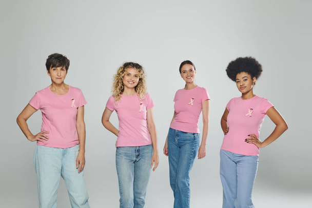 šťastný různé rasy ženy různého věku stojící na šedém pozadí, rakovina prsu, ruce v bok, póza - Fotografie, Obrázek