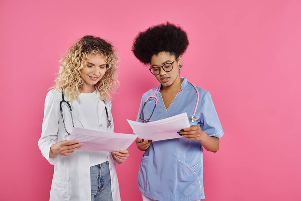 oncologistas felizes do sexo feminino, médicos inter-raciais em pano de fundo rosa, consciência do câncer de mama, diagnóstico - Foto, Imagem