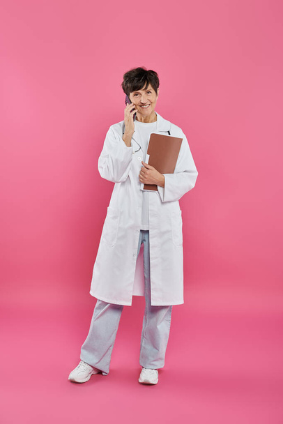 oncologo femminile, medico maturo che tiene la cartella e parla su smartphone, consapevolezza del cancro al seno - Foto, immagini