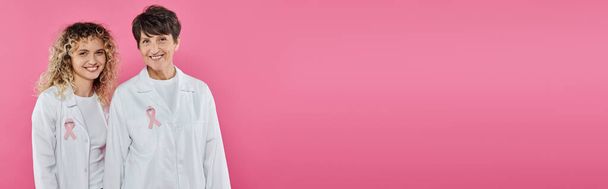 smiling doctors with ribbons on white coats isolated on pink, banner, breast cancer concept - Photo, Image