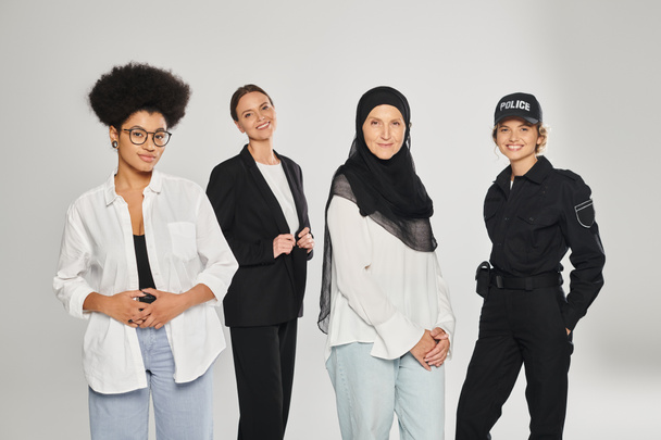 çok ırklı bir grup kadın kameraya bakıyor ve gri renkte poz verirken gülümsüyor. - Fotoğraf, Görsel