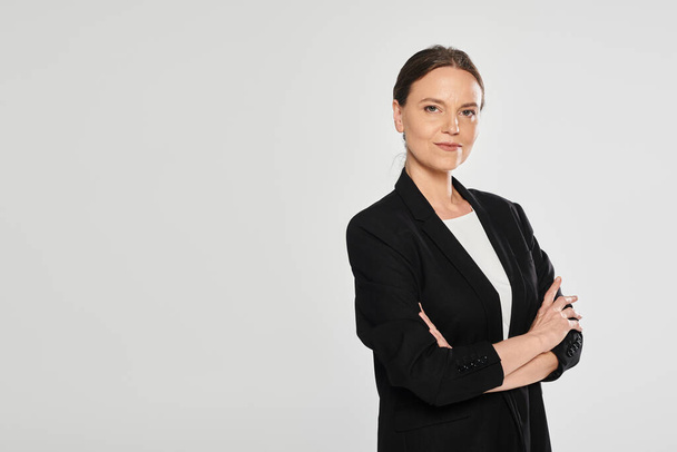 confident brunette woman in suit crossing arms and looking at camera isolated on grey - Photo, Image