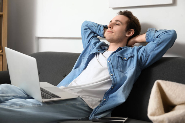 Muž na volné noze s notebookem odpočívá na pohovce doma - Fotografie, Obrázek
