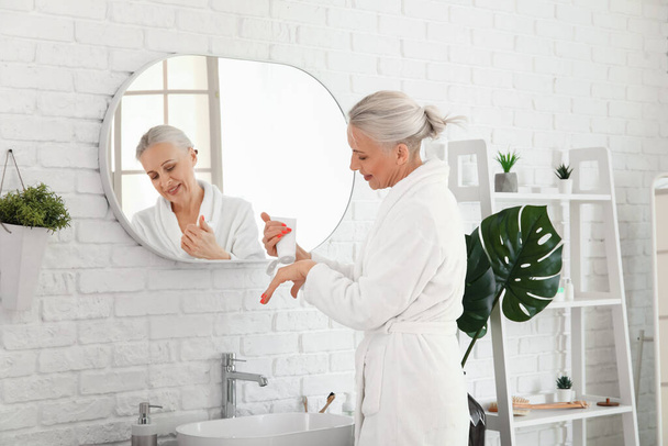 Reife Frau trägt Handcreme im Badezimmer auf - Foto, Bild