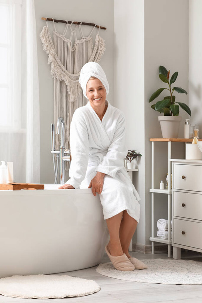 Зрелая женщина с полотенцем сидит в ванной комнате - Фото, изображение