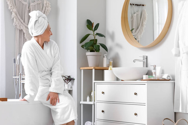 Mujer madura con toalla sentada en el baño - Foto, imagen