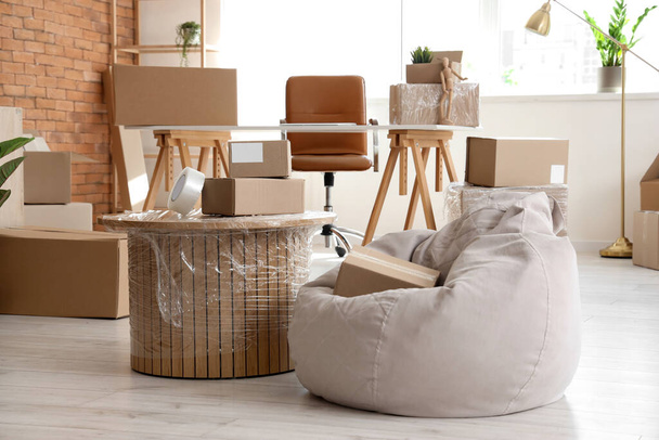 Coffee table and pouf with cardboard boxes in office on moving day - Photo, Image