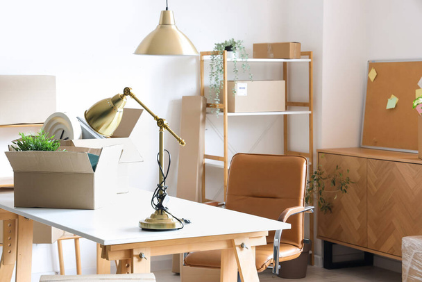 Modern workplace with lamp and cardboard boxes in office on moving day - Photo, Image