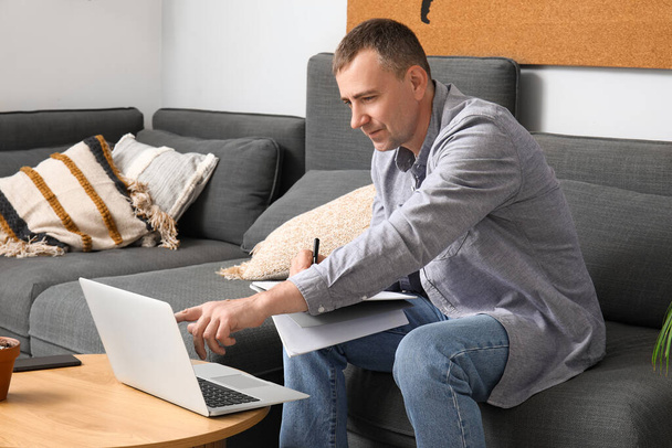 Mature male freelancer working with laptop on sofa at home - Photo, Image