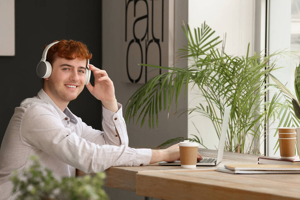 Male freelancer working with headphones and laptop at table in office - Photo, image