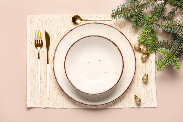 Table de Noël avec assiettes vides, couverts dorés et branches d'épinette sur fond rose - Photo, image