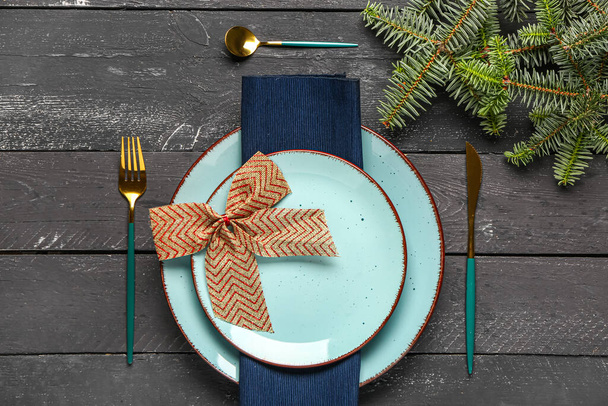 Weihnachtstisch mit Tannenzweigen, Besteck und schöner Schleife auf schwarzem Holzhintergrund - Foto, Bild