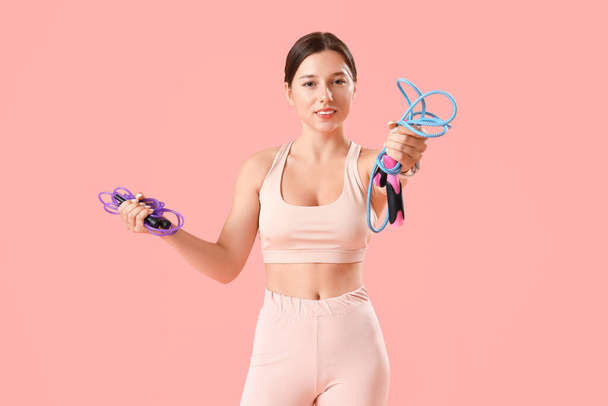 Sporty young woman with jumping ropes on pink background - Photo, Image