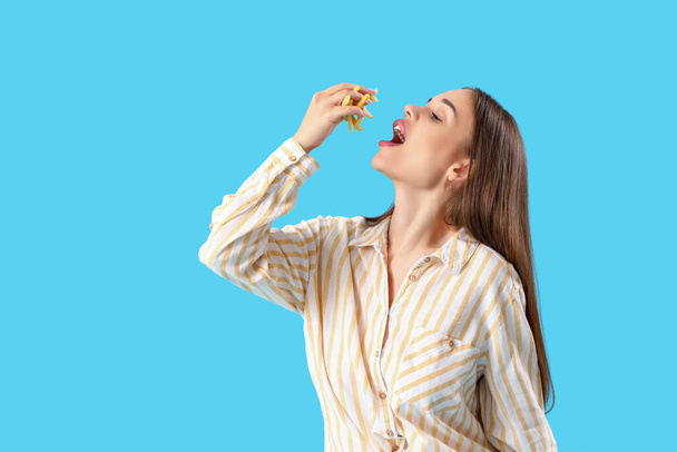 Красивая молодая женщина ест картошку фри на голубом фоне - Фото, изображение