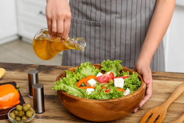 Vrouw toevoegen van olijfolie in kom met lekkere salade aan tafel in de keuken - Foto, afbeelding