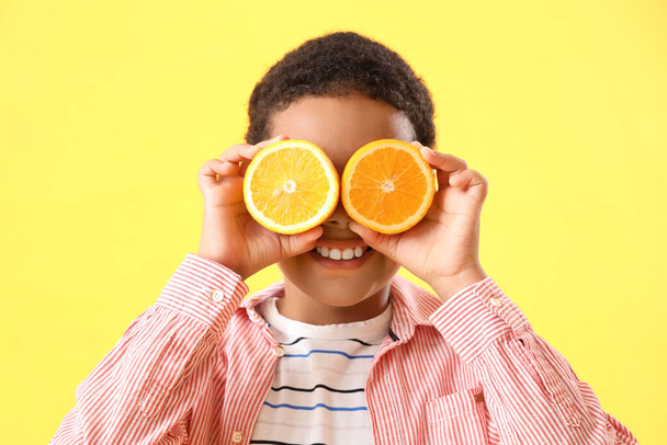黄色の背景にオレンジ色のスライスを持つ小さなアフリカ系アメリカ人の少年 - 写真・画像