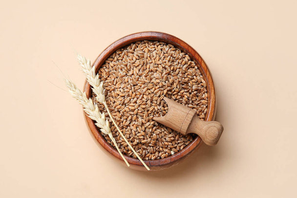 Дерев'яна миска з зернами, пшеничними вухами та соломою на бежевому фоні - Фото, зображення