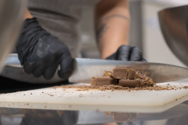 chef-kok snijden chocolade fudge snoep voor cheesecake voorbereiding close-up shots, cateraar professionele keuken - Foto, afbeelding