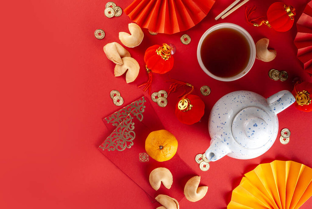 Chinese nieuwjaarsachtergrond. Rood en goudgeel plat met traditioneel Chinees nieuwjaarsdecor, enveloppen met wensen, gouden munten, waaiers, Chinese lantaarns, sinaasappels en thee - Foto, afbeelding