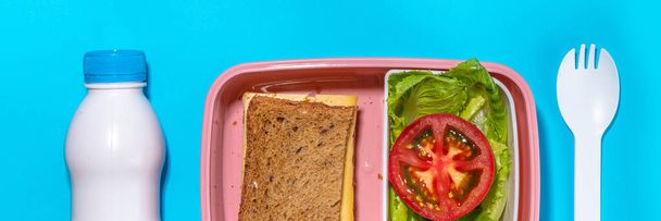 Healthy school meal, back to school concept. Children packed lunch box with balanced diet snack food - yogurt, cereal toast sandwich, apple, fresh vegetable salad, high-colored bright background - Fotó, kép