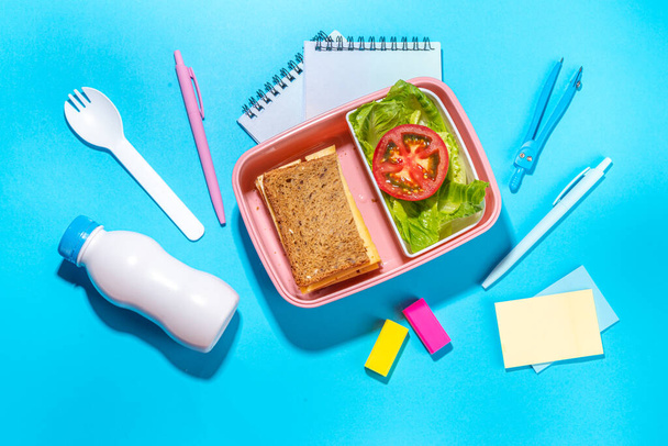 Healthy school meal, back to school concept. Children packed lunch box with balanced diet snack food - yogurt, cereal toast sandwich, apple, fresh vegetable salad, high-colored bright background - Photo, image