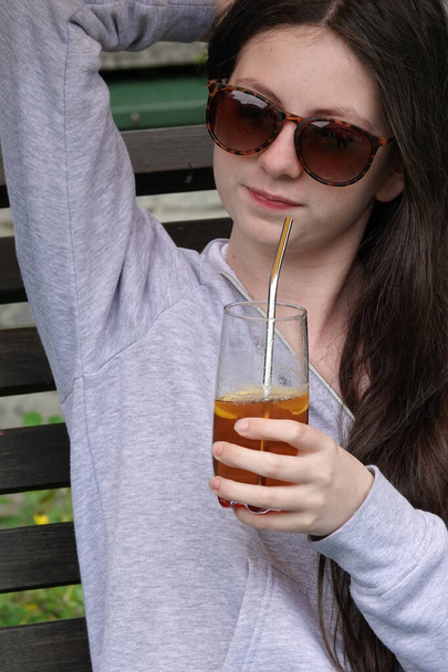 Adolescente de 14 ans avec des lunettes de soleil buvant du thé froid avec une paille en acier inoxydable - Photo, image
