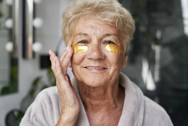 Donna caucasica anziana che applica una benda medica per gli occhi in bagno - Foto, immagini