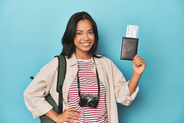 Filipina z aparatem fotograficznym, bilety, plecak na niebiesko pokazujący przestrzeń na dłoni i trzymający drugą rękę na pasie. - Zdjęcie, obraz