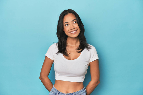 Filipina young woman on blue studio relaxed and happy laughing, neck stretched showing teeth. - Photo, Image