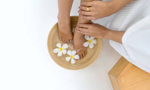 Female feet soaked in a bowl filled with water and flower petals, a depiction of relaxation and luxurious self-care. - Photo, Image