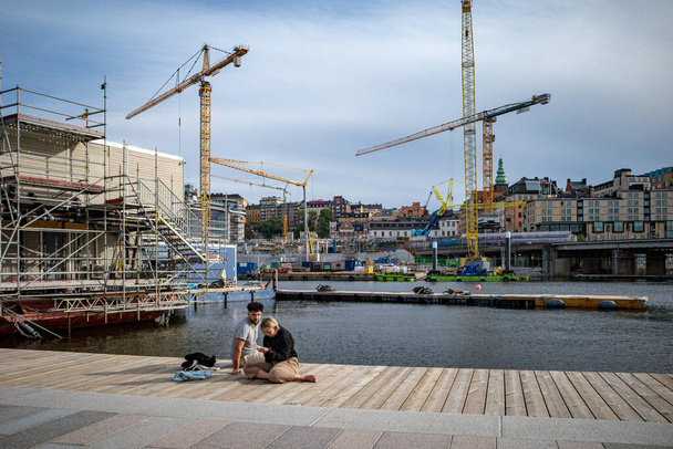 Estocolmo, Suécia 29 de agosto de 2023 Um jovem casal se senta à beira-mar no distrito de Slussen em meio à construção em grande escala. - Foto, Imagem