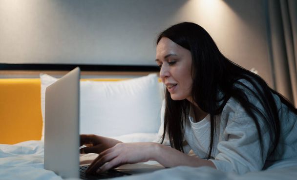 Mladá žena pomocí notebooku ležící v posteli, sledovat film nebo prohlížení sociálních médií. - Fotografie, Obrázek